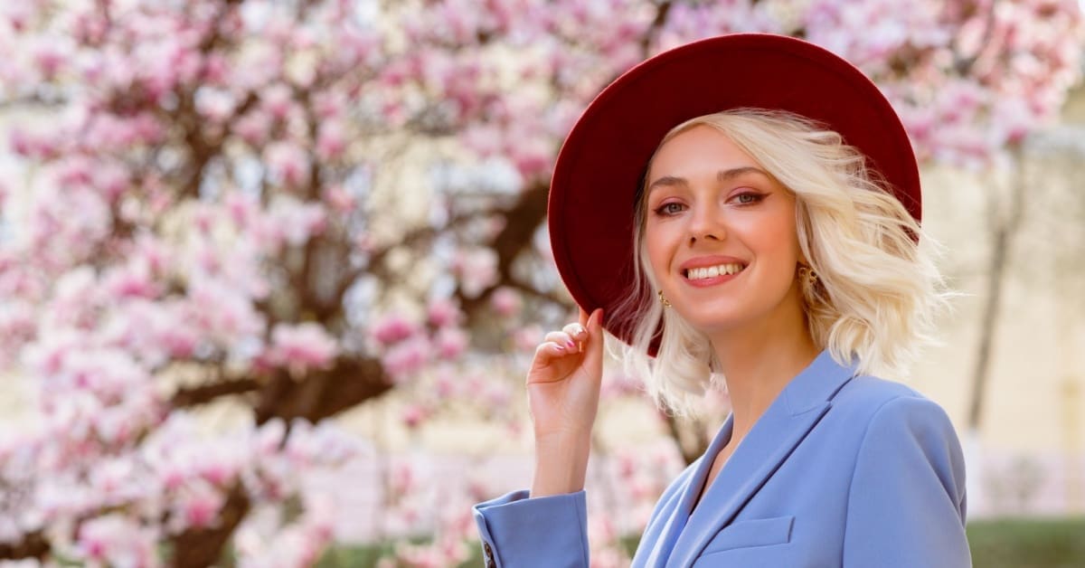 young woman smiling with hat and flowers in background, concept of link between oral hygiene and luxury fashion